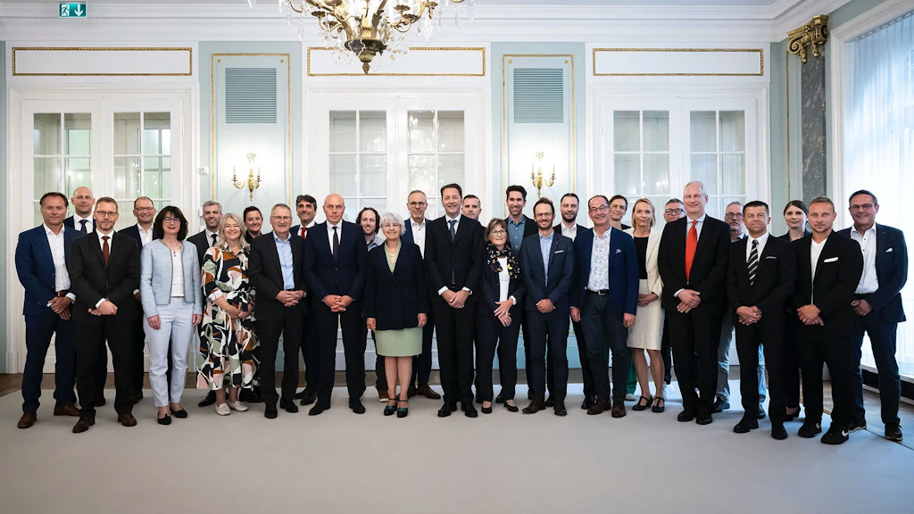 Eine Gruppe von rund dreissig Personen steht nebeneinander und posiert für ein Gruppenfoto anlässlich eines runden Tisches zur Erklärung von Mailand. Der helle Raum hat hohe Fenster und einen Kronleuchter.